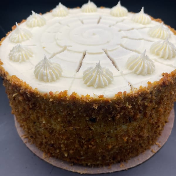 A round carrot cake with white cream cheese frosting, decorated with piped rosettes and pre-sliced.