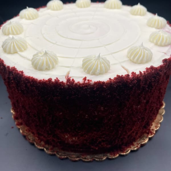 A whole red velvet cake with white cream cheese frosting and decorative dollops on top.