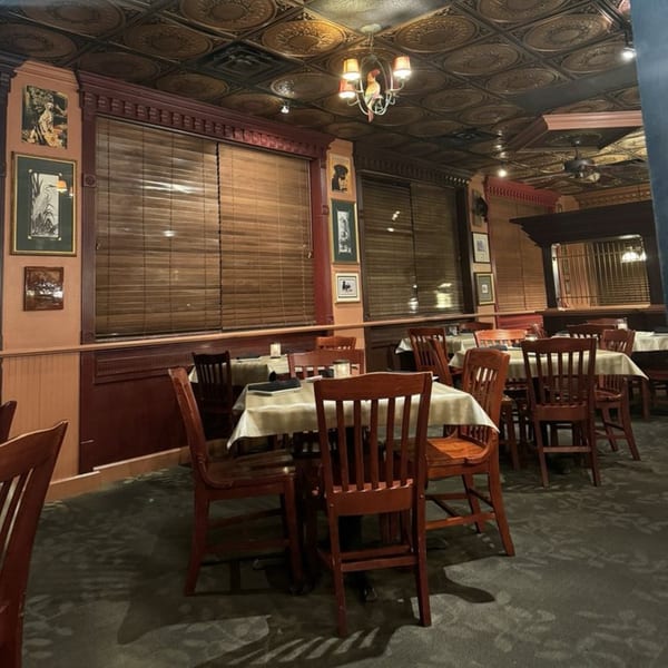 Dining room at Ducks Grille & Bar with wooden chairs, white tablecloths, and patterned ceiling.