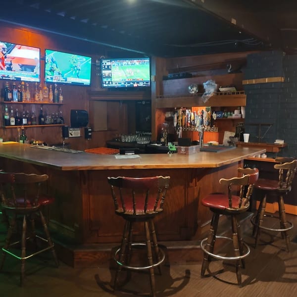 Ducks Grille & Bar interior with a long wooden bar, stools, and multiple TVs showing sports.