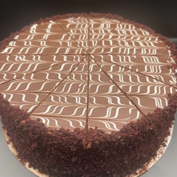 A chocolate cake with white icing swirls on top, pre-sliced into wedges, and chocolate crumbs on the sides.
