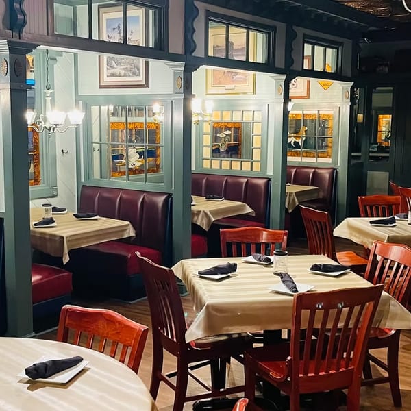 Interior of Ducks Grille & Bar, featuring red booths, wooden chairs, and tables with light tablecloths.